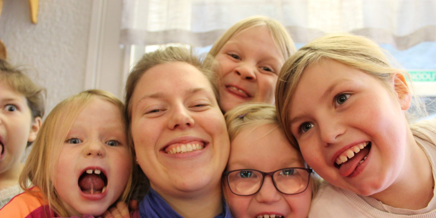 Bilde: Flere barn smiler og gjør grimaser, sammen med lederen sin. Bildet er en selfie.